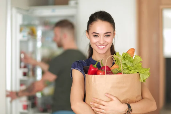 Jovem casal na cozinha, mulher com um saco de compras — Fotografia de Stock