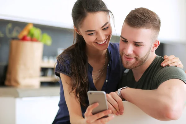 Pareja feliz usando smartphone sentado en la cocina —  Fotos de Stock