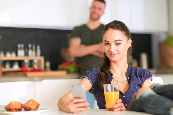 Casal feliz usando smartphone sentado na cozinha — Fotografia de Stock