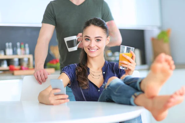 台所に座っているスマート フォンを使用して幸せなカップル — ストック写真