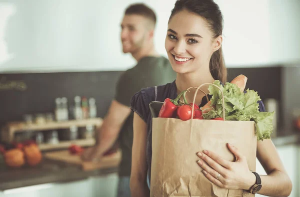 Unga par i köket, kvinna med en påse livsmedel shopping — Stockfoto