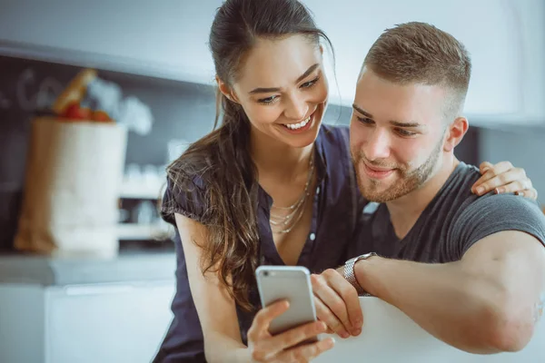 Pareja feliz usando smartphone sentado en la cocina — Foto de Stock