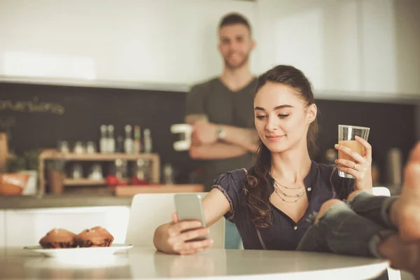 Pareja feliz usando smartphone sentado en la cocina —  Fotos de Stock