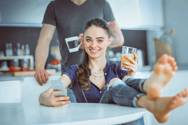 Pareja feliz usando smartphone sentado en la cocina — Foto de Stock