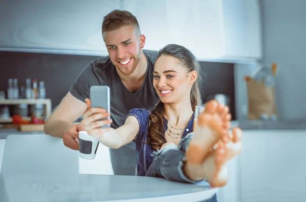 Glückliches Paar sitzt mit Smartphone in Küche — Stockfoto