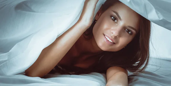 Giovane bella donna sdraiata a letto sotto copertura — Foto Stock