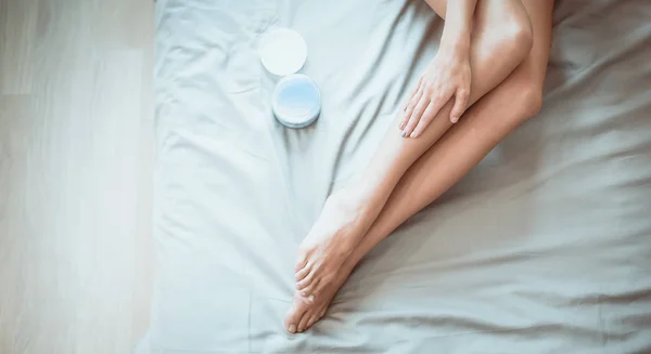 Bella donna seduta sul letto e applicare la crema sulle gambe — Foto Stock