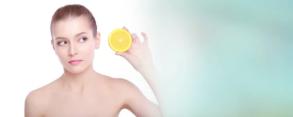 Beautiful young shirtless woman holding piece of orange in front of her eye while standing against white background — Stock Photo, Image