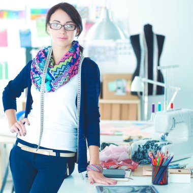 Güzel moda tasarımcısı stüdyoda masanın yanında duruyor.