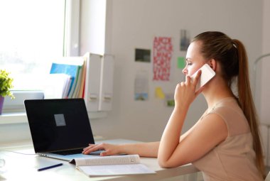 Genç iş kadını masada oturuyor ve telefonla konuşuyor.