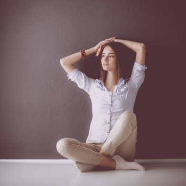 Genç bir kadın yerde, kara duvarın yanında oturuyor.