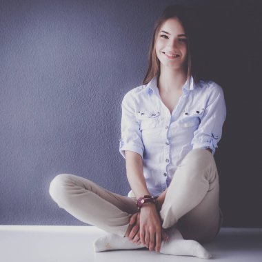 Genç bir kadın yerde, kara duvarın yanında oturuyor.