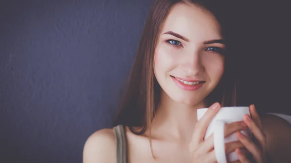 Krásná mladá žena s šálkem kávy na hnědé pozadí — Stock fotografie