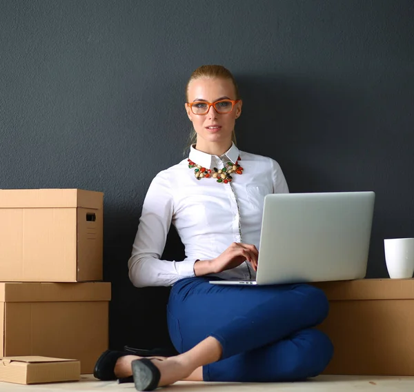 Женщина сидит на полу рядом с коробками с ноутбуком — стоковое фото