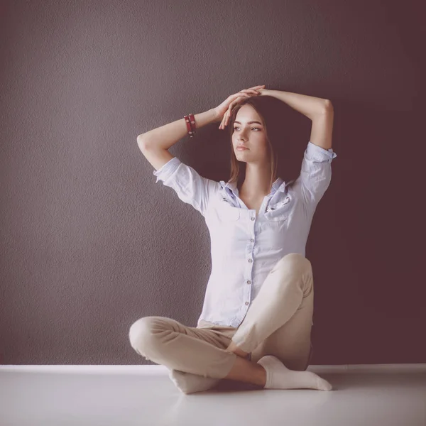 Giovane donna seduta sul pavimento vicino al muro scuro — Foto Stock