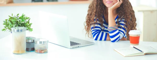 Smiling young woman with coffee cup and laptop in the kitchen at home — Stock Photo, Image