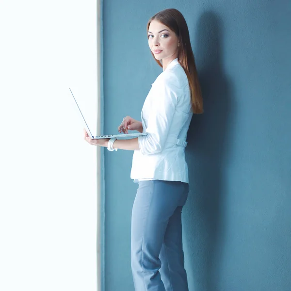 Mujer joven sosteniendo un ordenador portátil, de pie sobre fondo gris —  Fotos de Stock