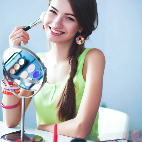 Joven hermosa mujer haciendo maquillaje cerca del espejo, sentado en el escritorio — Foto de Stock