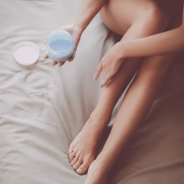 Vacker kvinna sitter på sängen och tillämpa kräm på ben — Stockfoto