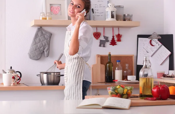 Portret van een lachende vrouw met telefoon in de keuken thuis — Stockfoto