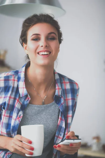 Retrato de una mujer joven usando el teléfono móvil mientras desayunaba en la cocina en casa — Foto de Stock