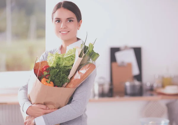 Ung kvinna som håller i matkassen med grönsaker. Stående i köket — Stockfoto