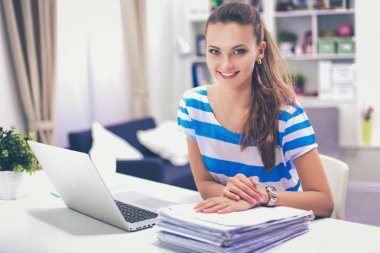 Elinde evrakları olan kadın masanın üstünde oturuyor.