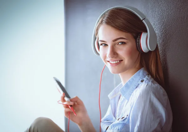 Ragazza sorridente con le cuffie seduto sul pavimento vicino al muro — Foto Stock