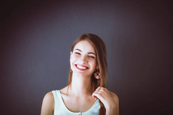 Joven mujer sonriente de pie cerca de la pared oscura —  Fotos de Stock