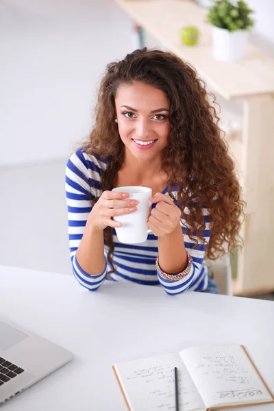 Souriant jeune femme avec tasse de café et ordinateur portable dans la cuisine à la maison — Photo