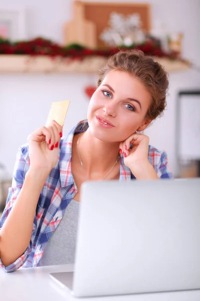 Mujer sonriente compras en línea utilizando la computadora y la tarjeta de crédito en la cocina — Foto de Stock