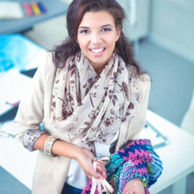 Gülümseyen kadın moda tasarımcısı ofis masasında oturuyor.