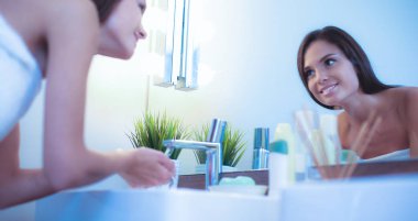 Genç bir kadın banyoda yüzünü temiz suyla yıkıyor.