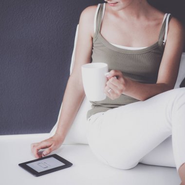 Kupası ve tablet duvarının yakınında katta oturan çekici beyaz kız