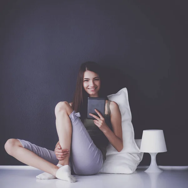 Mujer morena bonita sentada en el suelo con una almohada y mesa de avión — Foto de Stock