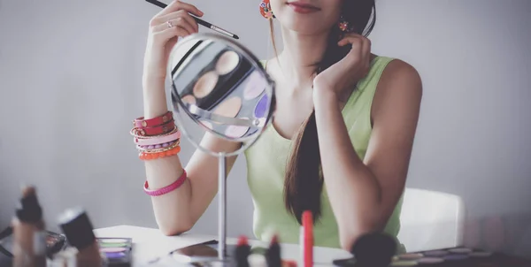 Nuori kaunis nainen tekee meikkiä lähellä peiliä, istuu pöydällä — kuvapankkivalokuva