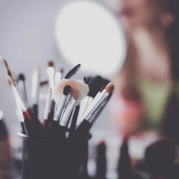 Joven hermosa mujer haciendo maquillaje cerca del espejo, sentado en el escritorio —  Fotos de Stock