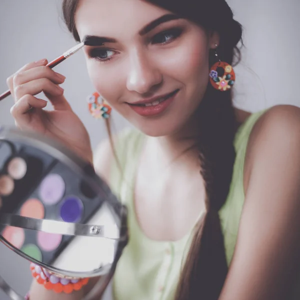 Junge schöne Frau schminkt sich in der Nähe des Spiegels und sitzt am Schreibtisch — Stockfoto