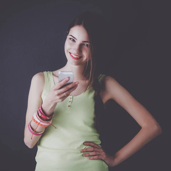 Beautiful businesswoman using cell phone standing near wall — Stock Photo, Image