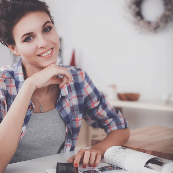 Portret van een jonge vrouw met behulp van mobiele telefoon tijdens het ontbijten in de keuken thuis — Stockfoto