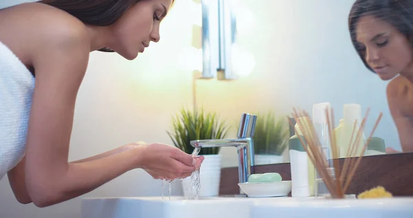 Mujer joven lavándose la cara con agua limpia en el baño —  Fotos de Stock