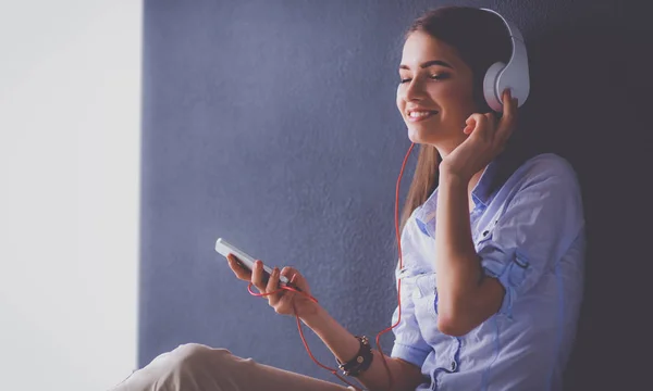 Smiling girl with headphones sitting on the floor near wall