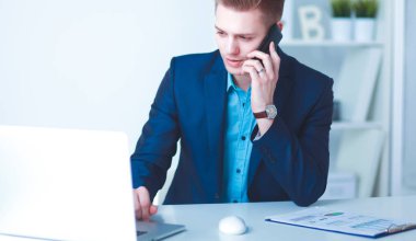 Genç işadamı ofiste çalışıyor, masada oturuyor.