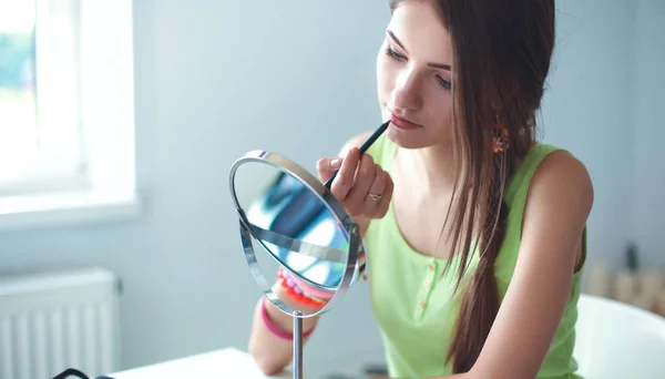 Joven hermosa mujer haciendo maquillaje cerca del espejo, sentado en el escritorio — Foto de Stock