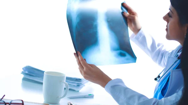 Mladá doktorka studující rentgenový snímek, sedí za stolem — Stock fotografie