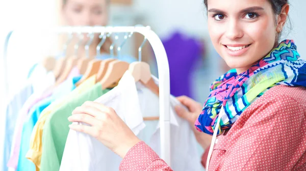Beautiful young stylist near rack with hangers in office — Stock Photo, Image