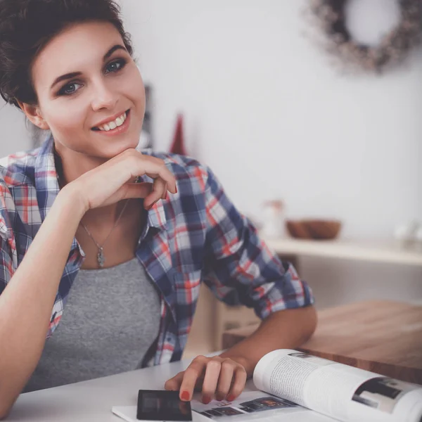 Portret van een jonge vrouw met behulp van mobiele telefoon tijdens het ontbijten in de keuken thuis — Stockfoto