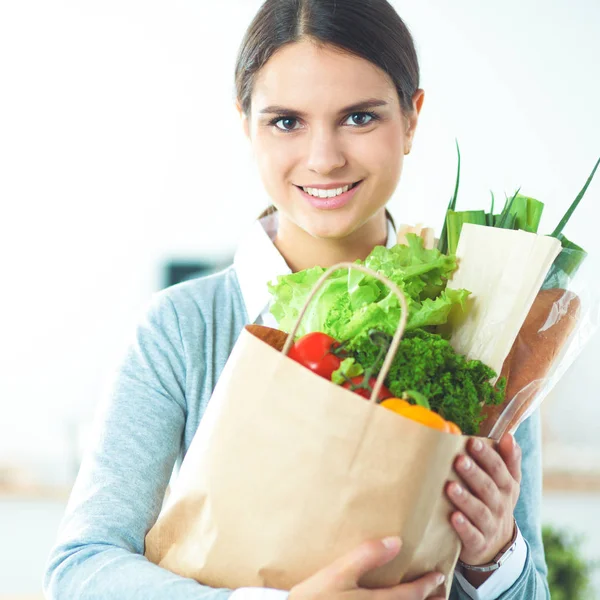 Jovem segurando supermercado saco de compras com legumes de pé na cozinha. — Fotografia de Stock