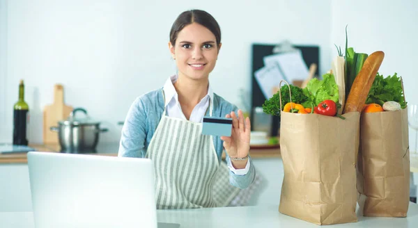 Mutfakta bilgisayar ve kredi kartı kullanan gülümseyen bir kadın. — Stok fotoğraf