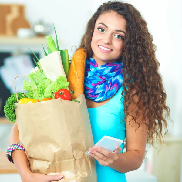 Glimlachende vrouw met mobiele telefoon houden boodschappentas in de keuken — Stockfoto
